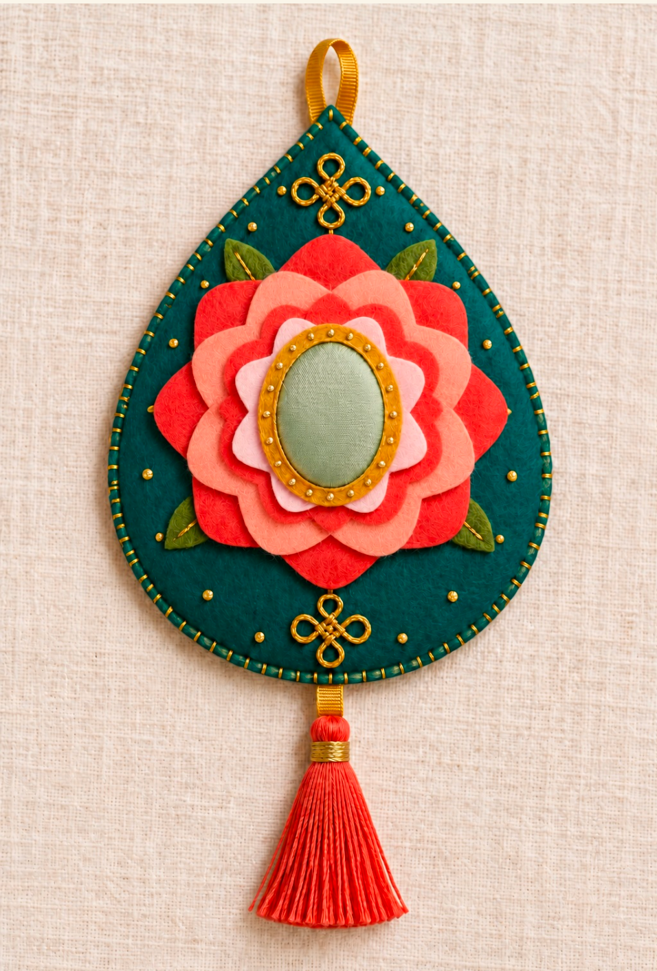 Lucky Pendant craft design: a dark green teardrop-shaped felt ornament with a layered coral flower, oval centre and red tassel.