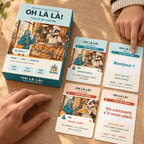 Hands beside the Oh Là Là! box and paired bakery and greeting cards on a wooden table, with one finger pointing to 'Bonjour!'
