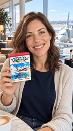 Woman holding the VOYAGE Inflight Edition box in an airport café, with an aeroplane outside the window.
